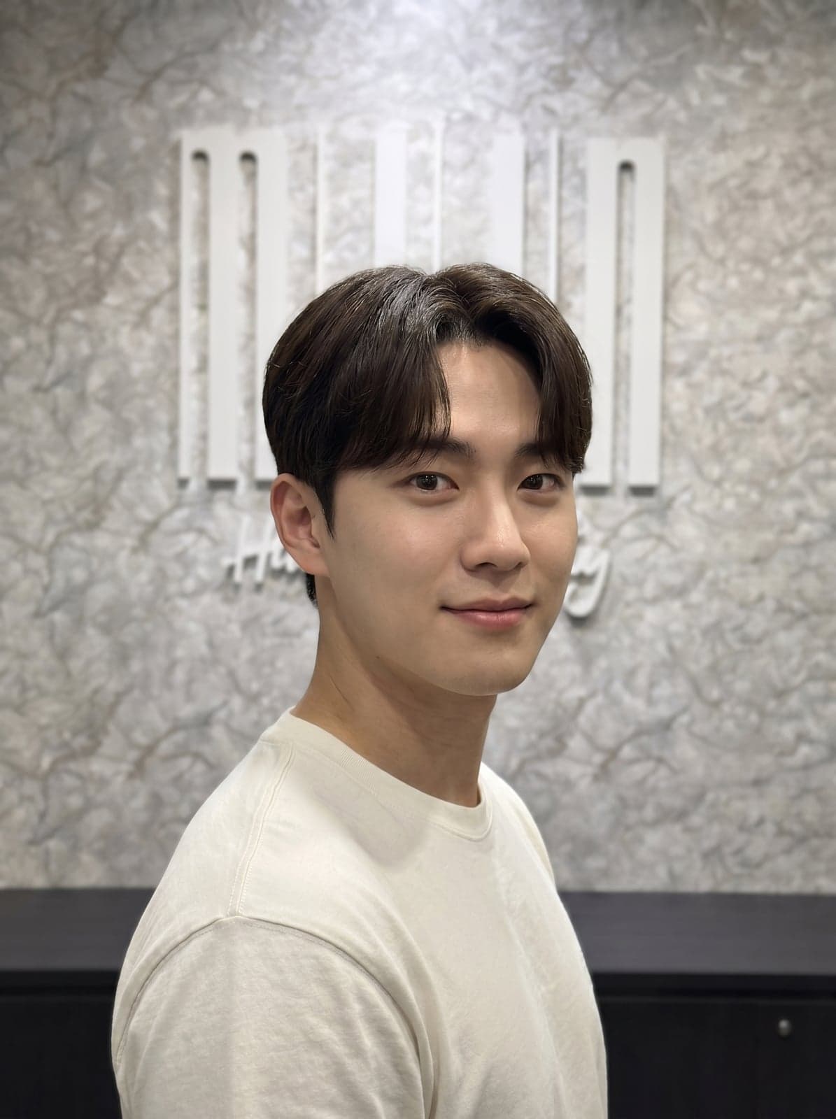 Two block dengan middle part — belahan tengah dengan poni curtain yang jatuh natural di kedua sisi, model rambut Korea pria low-maintenance